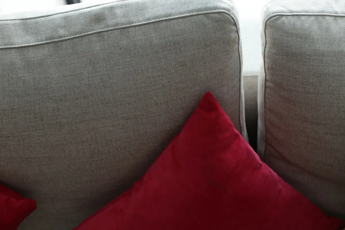 A single red cushion on a soft gray sofa