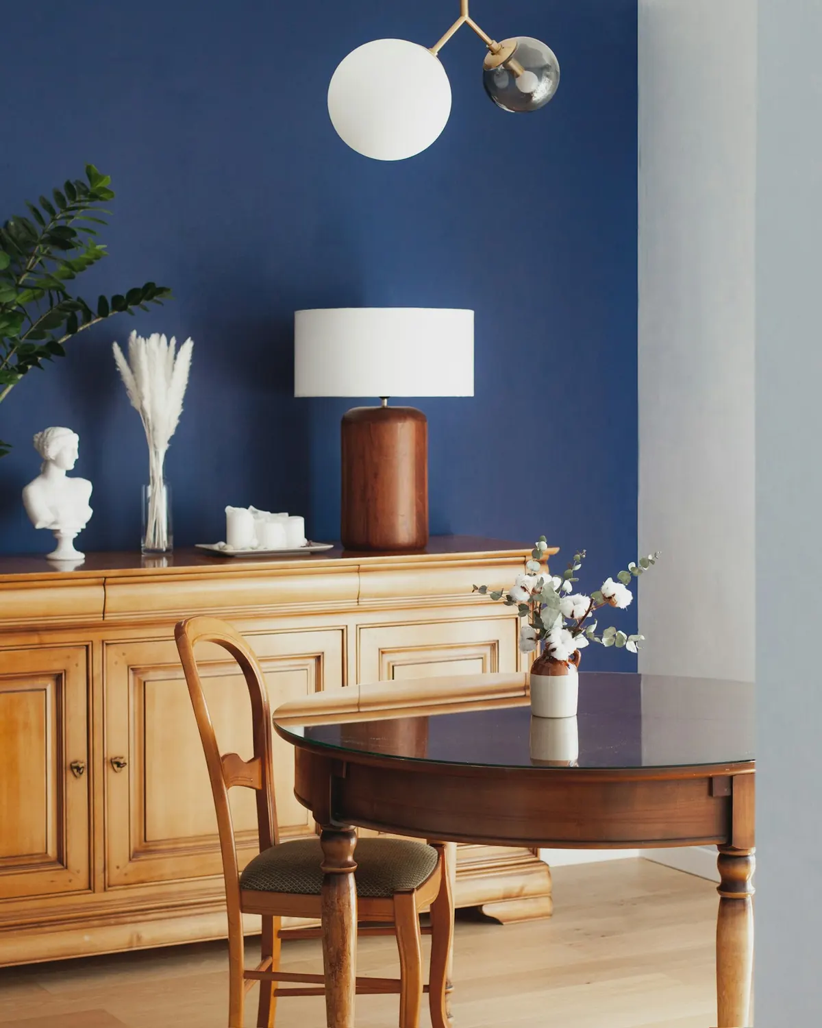 A blue wall with warm wooden furniture and a brown lamp