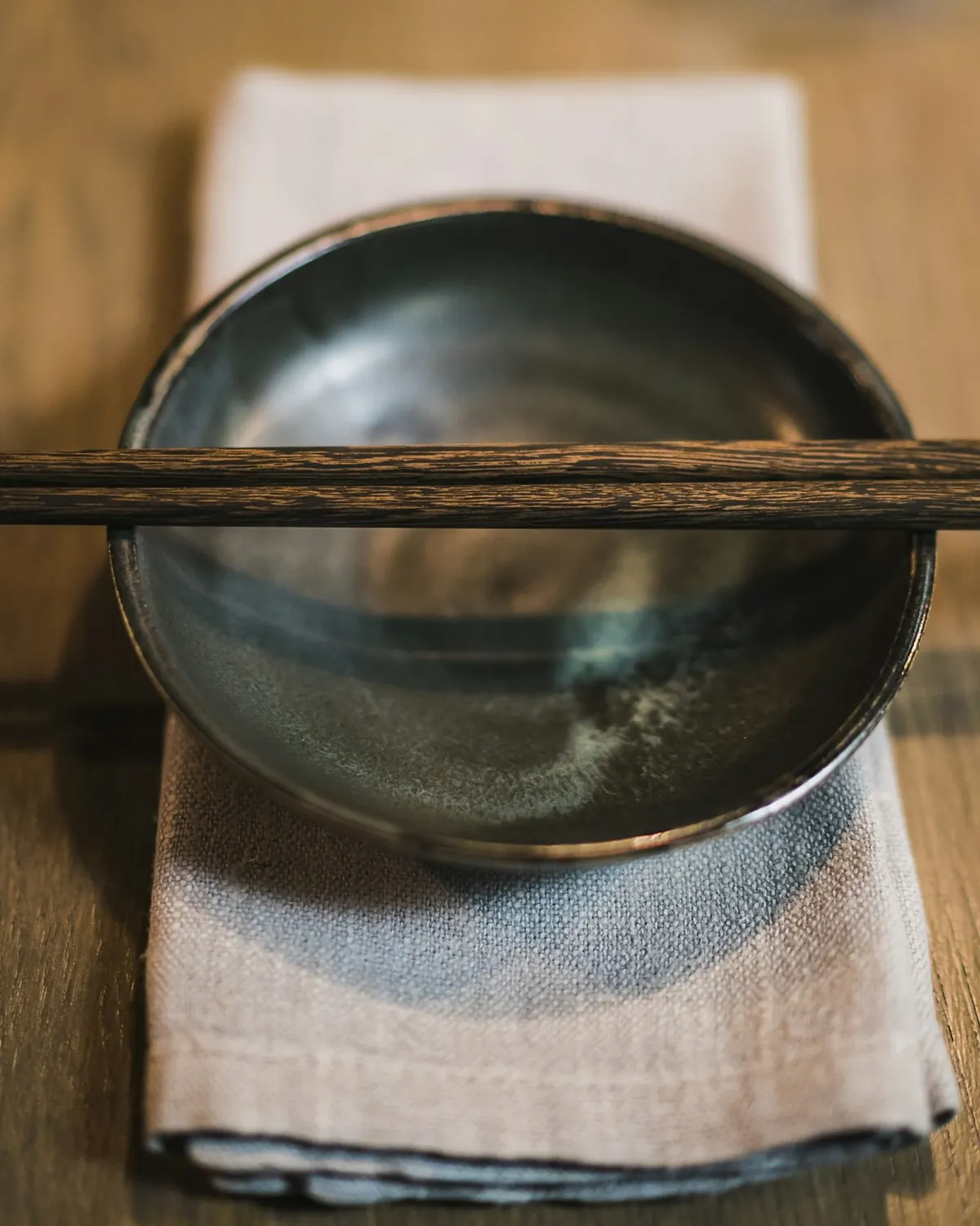 A dark ceramic bowl on oat-colored linen and wood