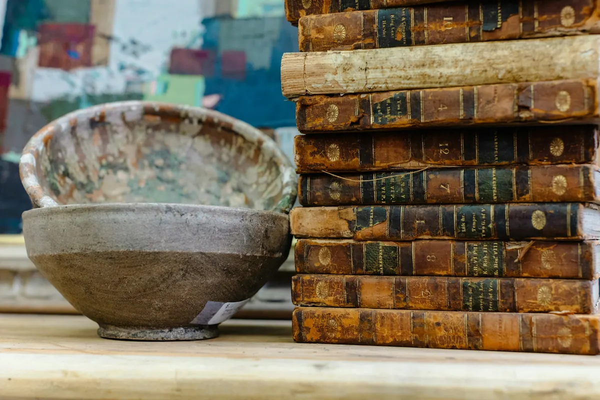 Old leather-bound books stacked beside rustic ceramic bowls