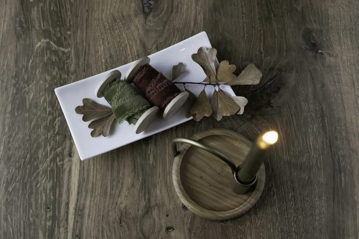 Burgundy ribbon, dried leaves and candlelight on dark wood