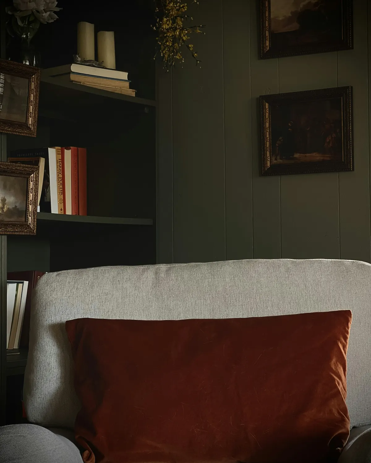 A deep red cushion on a cream sofa before dark wooden shelves