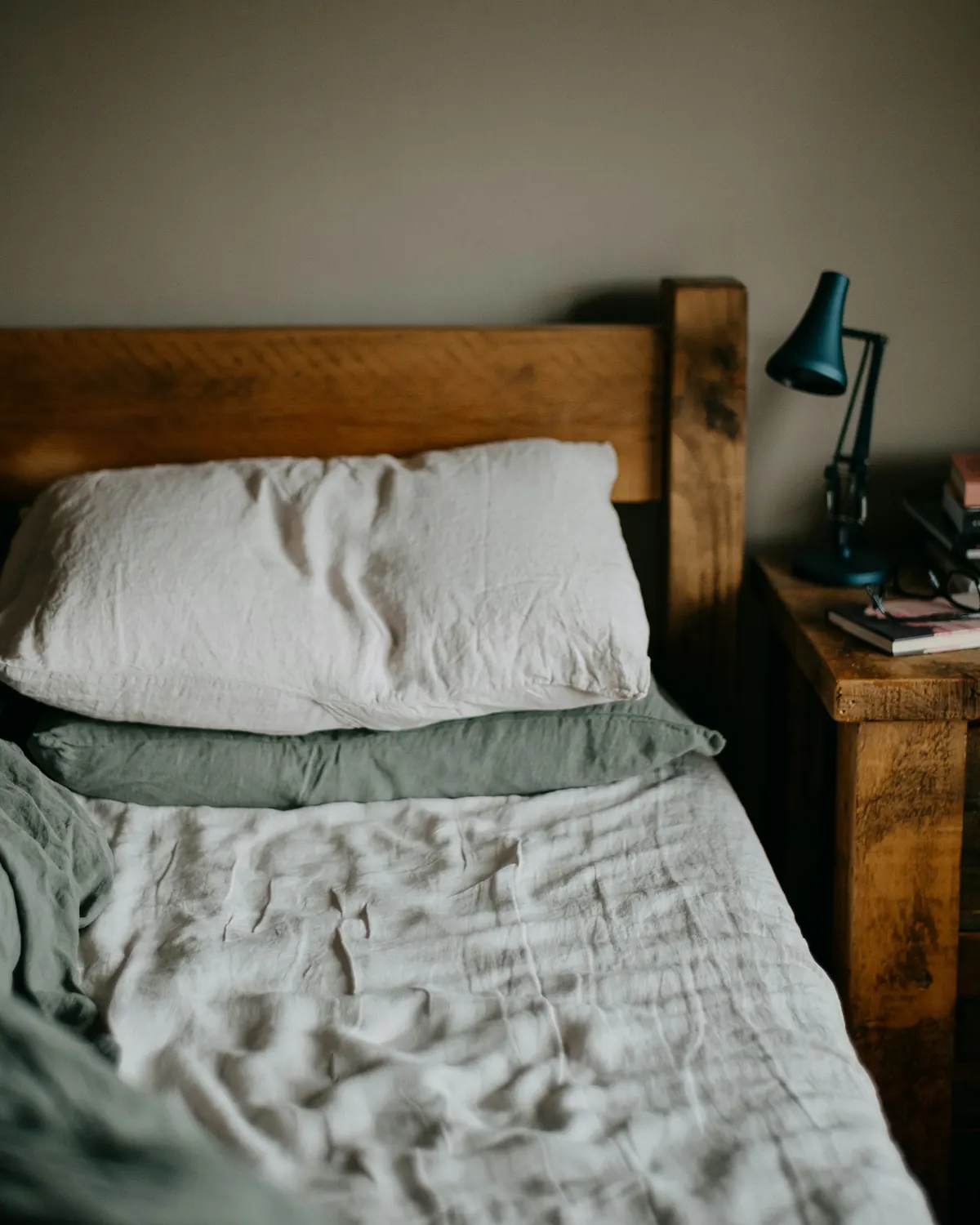 A relaxed linen bed with rumpled sheets and a wooden frame