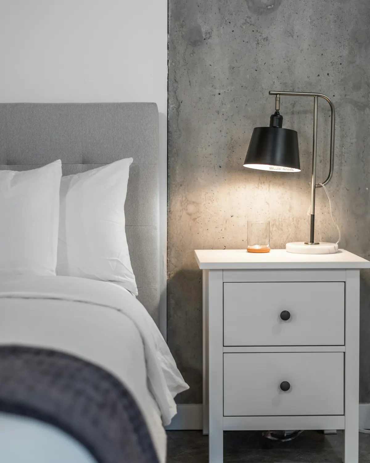 A neatly made bed beside a square white bedside table