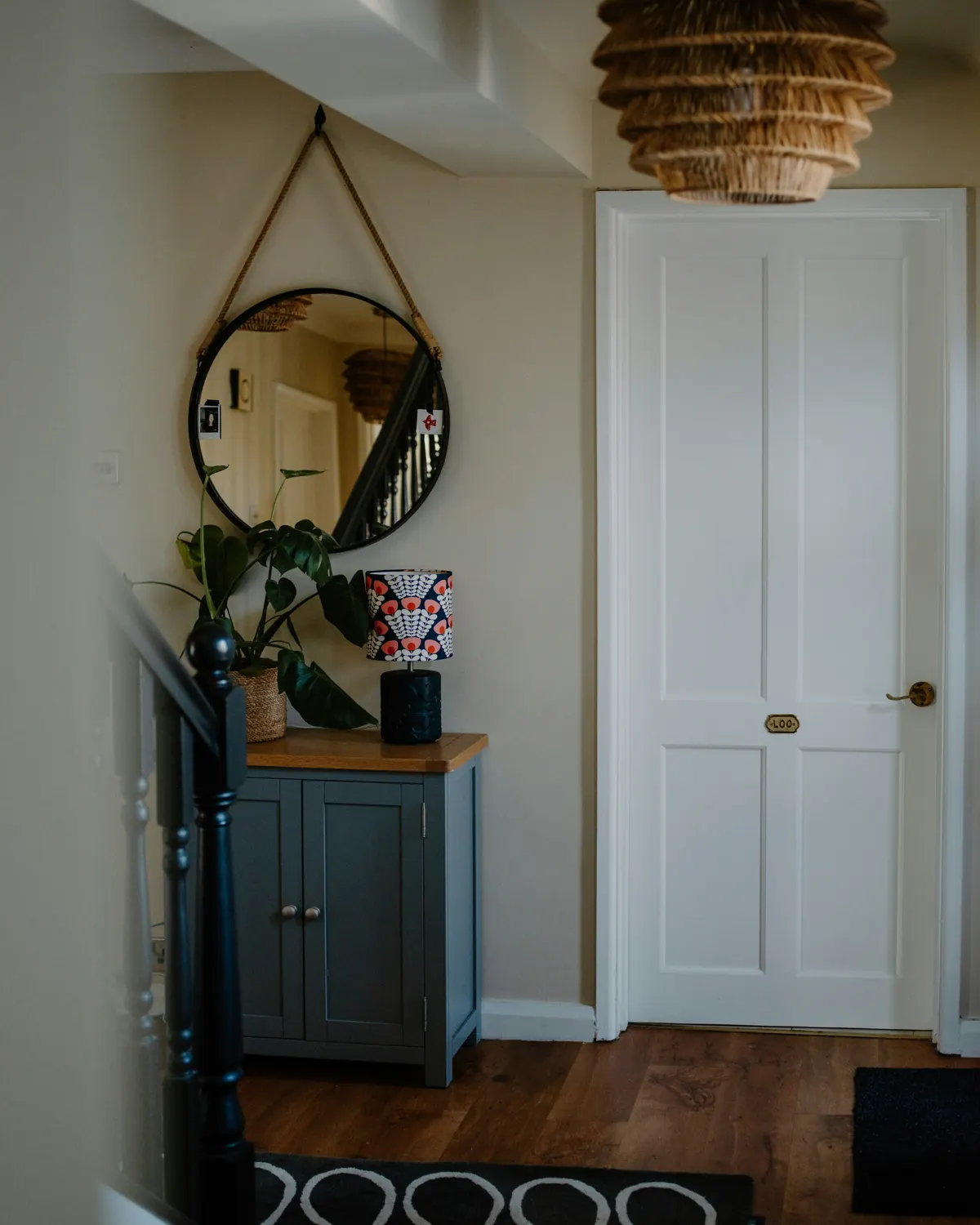 A narrow entryway with a cabinet and a round mirror