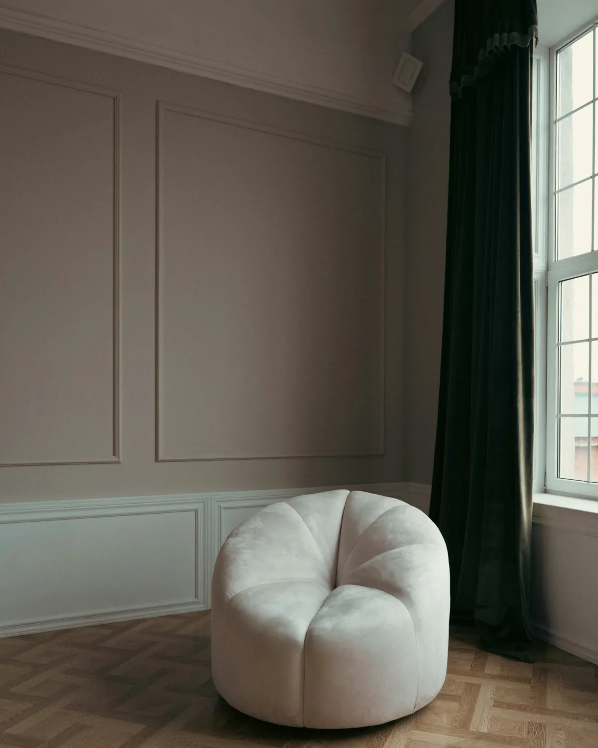 A rounded cream armchair in a paneled room