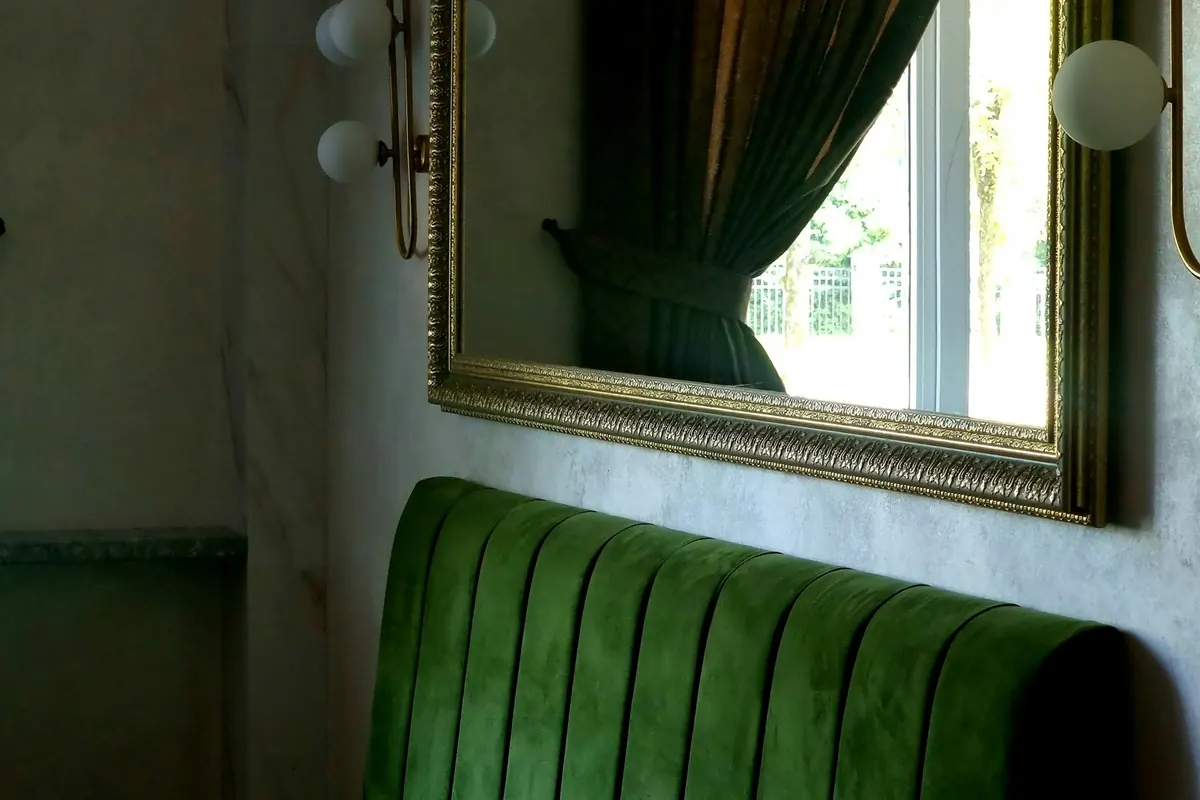 A green velvet banquette beneath a gilt-framed mirror
