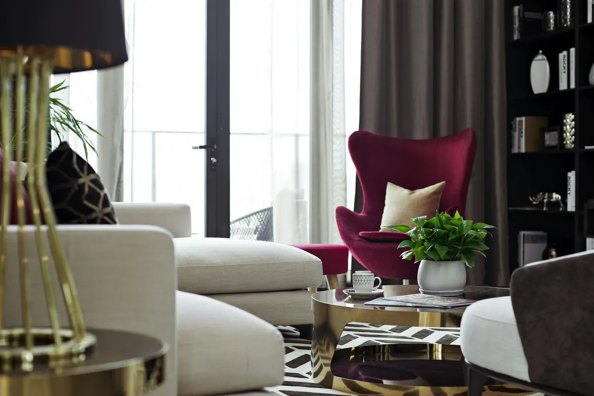 A living room with a burgundy wingback chair, cream sofas and brass details
