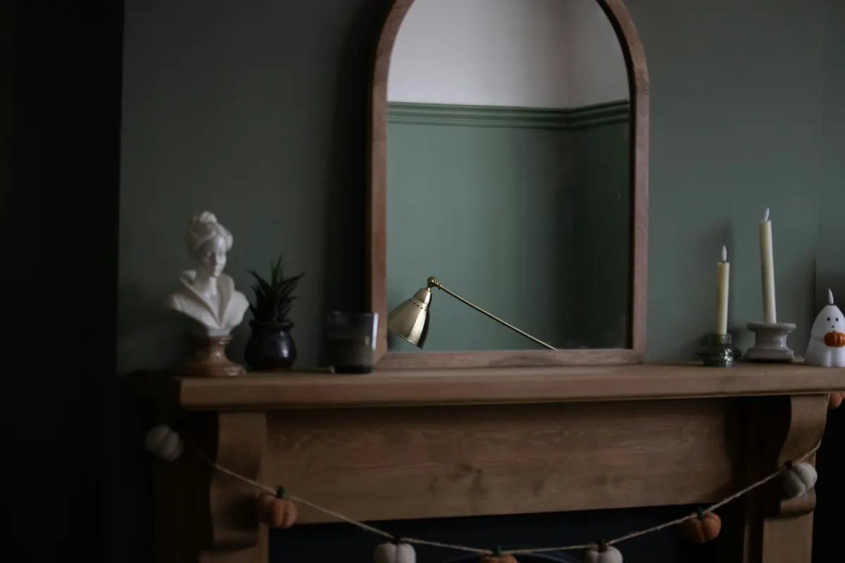 An arched mirror above a wooden mantel against a green wall