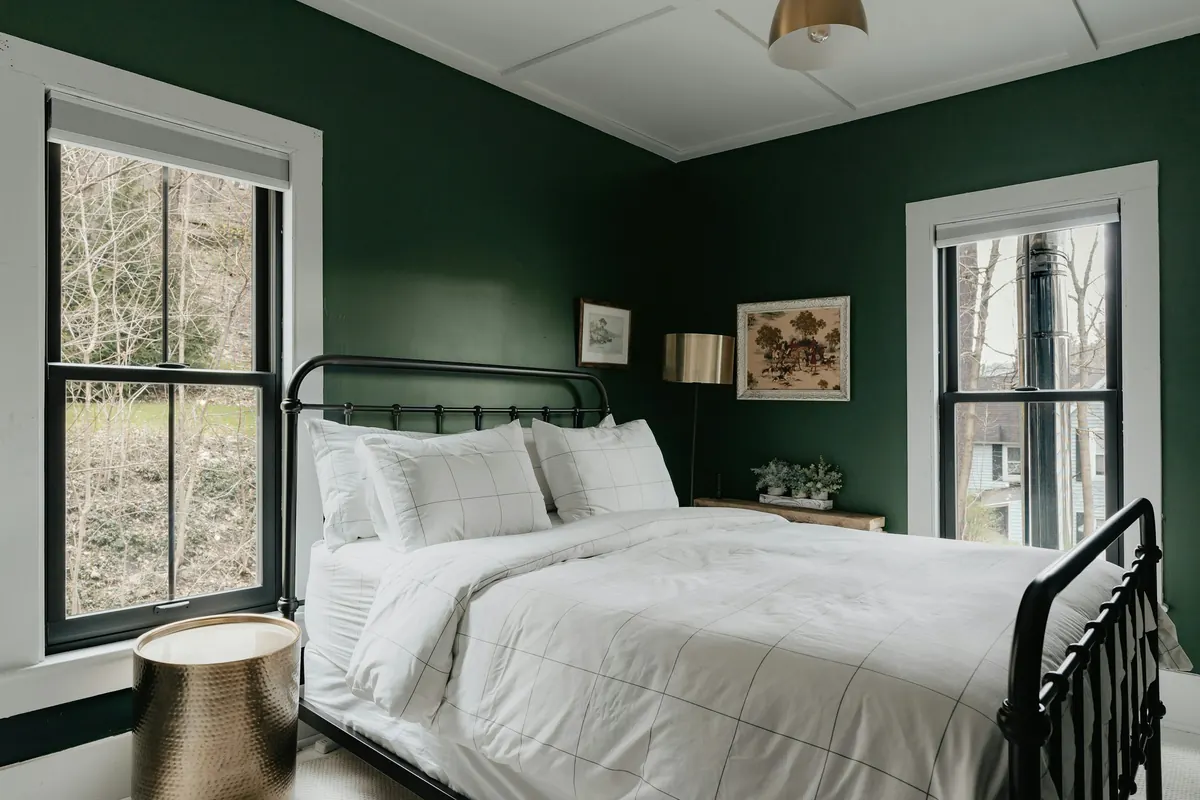 A bedroom painted deep green, with white bedding