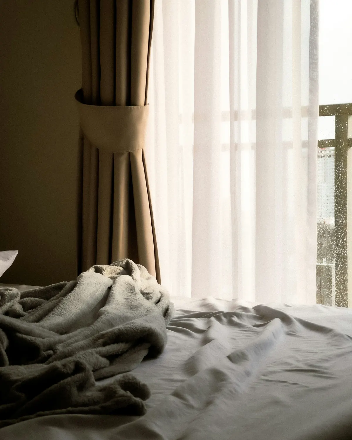 Early daylight falling across an unmade bed and linen curtains