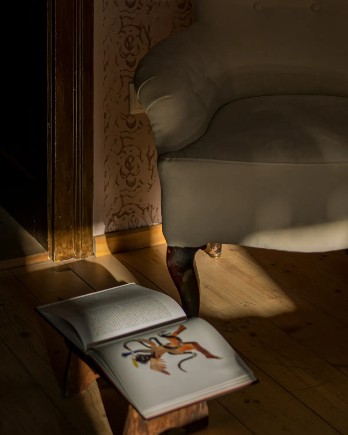 An open book in a pool of light beside an armchair