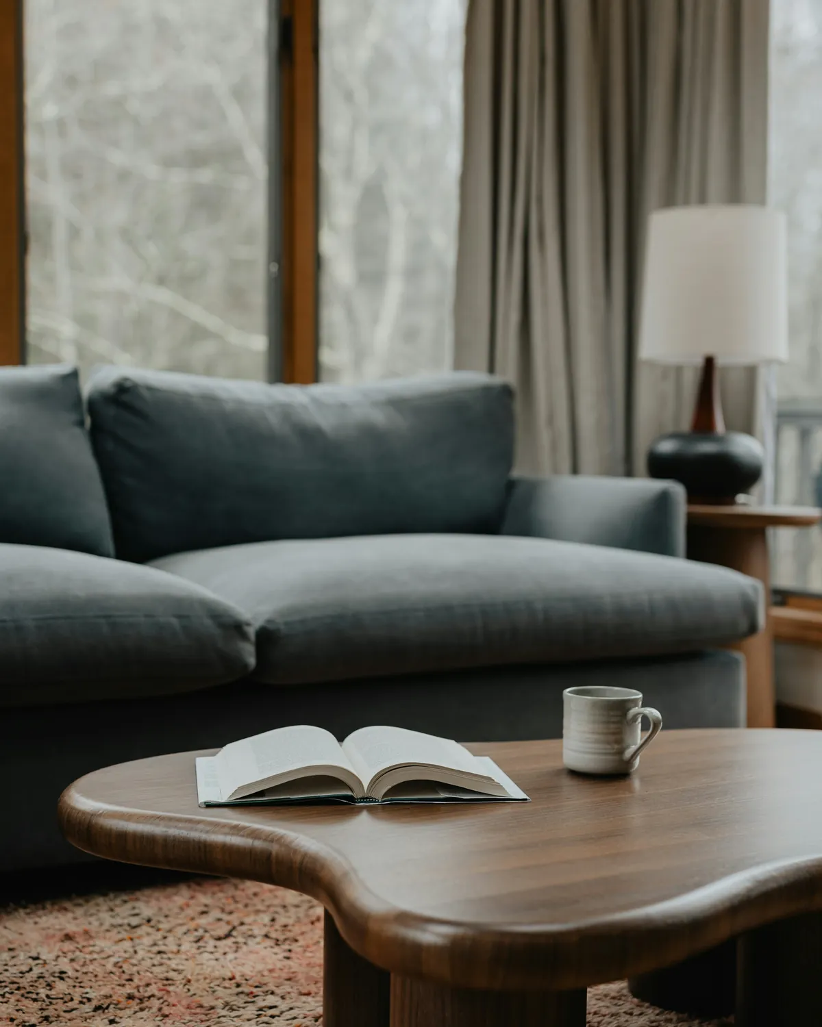 Open book and cup on a wooden coffee table in front of a sofa
