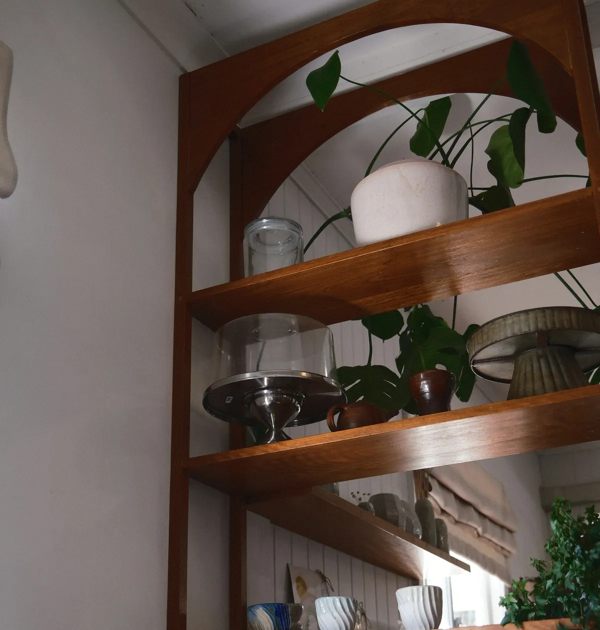 Arched wooden shelves with ceramics, glass and plants