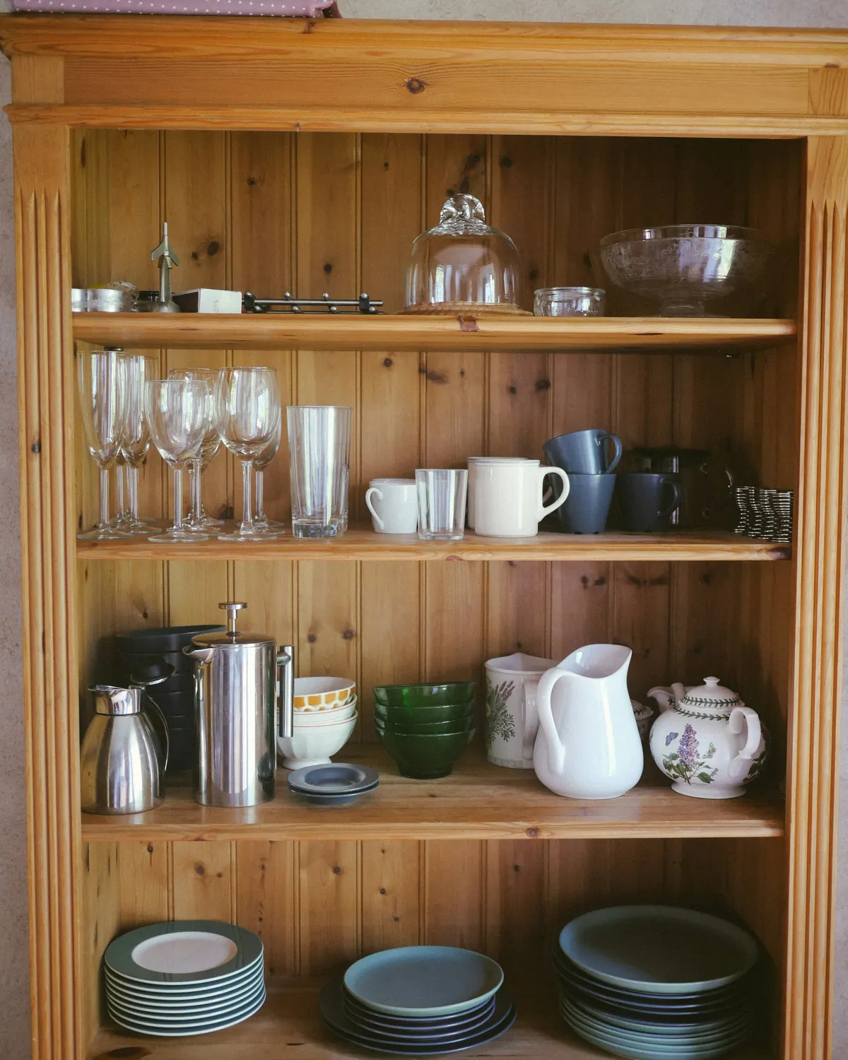 A wooden kitchen cabinet with pitchers, cups and plates
