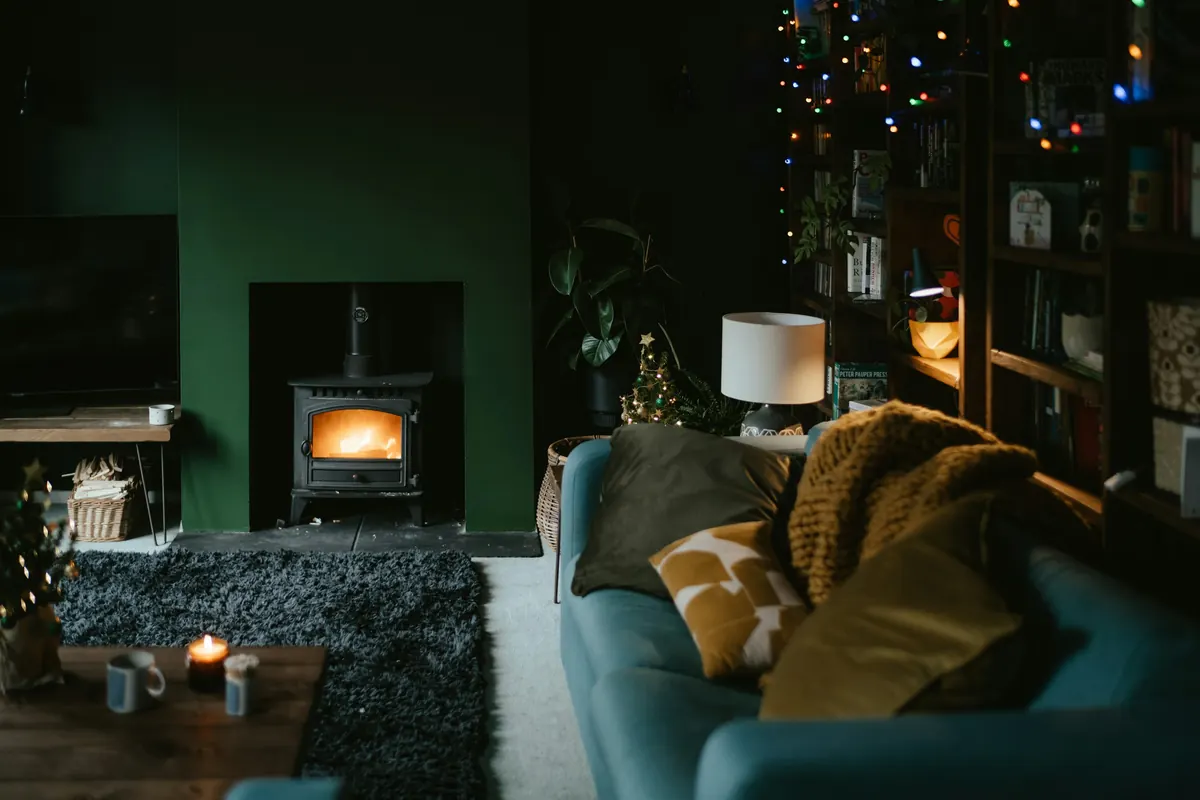 A cozy living room at dusk with a wood stove, lamps and a velvet sofa