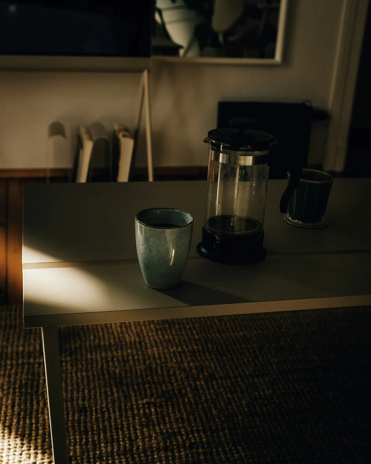A ceramic mug and a coffee press in soft kitchen light