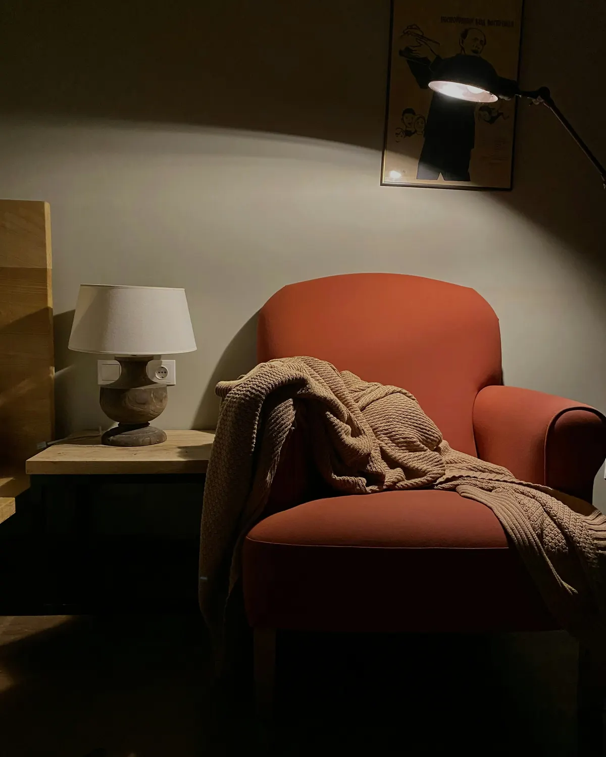A terracotta armchair with a knitted throw and a table lamp
