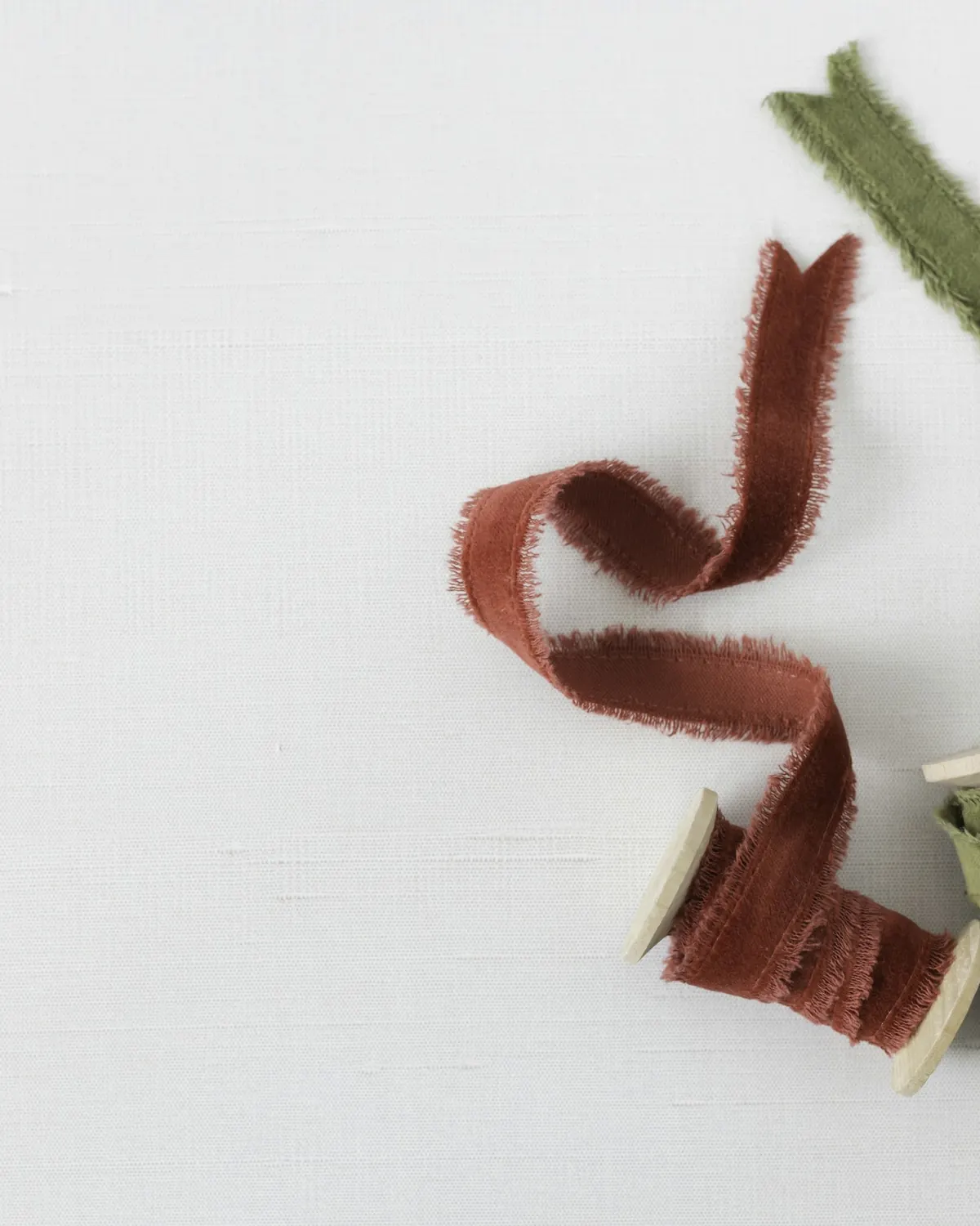 A length of rust-red silk ribbon on a pale surface