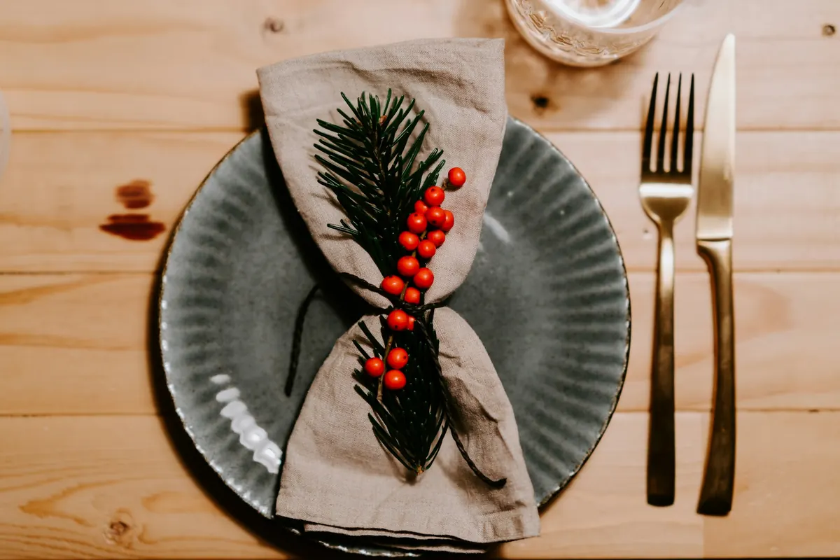 A linen napkin with a sprig of green on a plate, beside a fork and knife